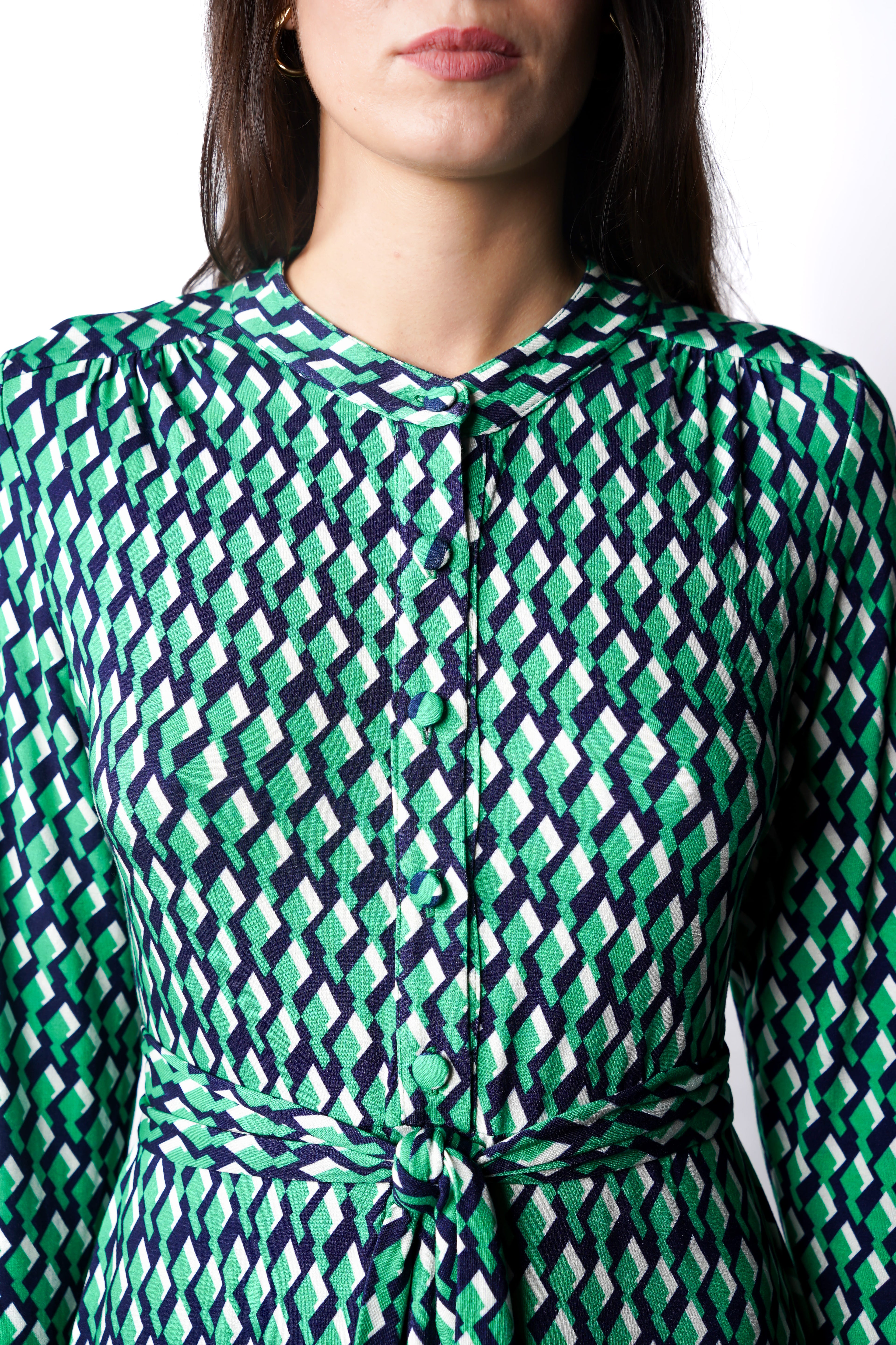 Robe à motif géométrique vert mi-longue à l’élégance naturelle. Col chemisier, boutonnage intégral et poche poitrine boutonnée. Bas légèrement évasé et ceinture amovible à nouer pour structurer la silhouette. Fabriquée en France.