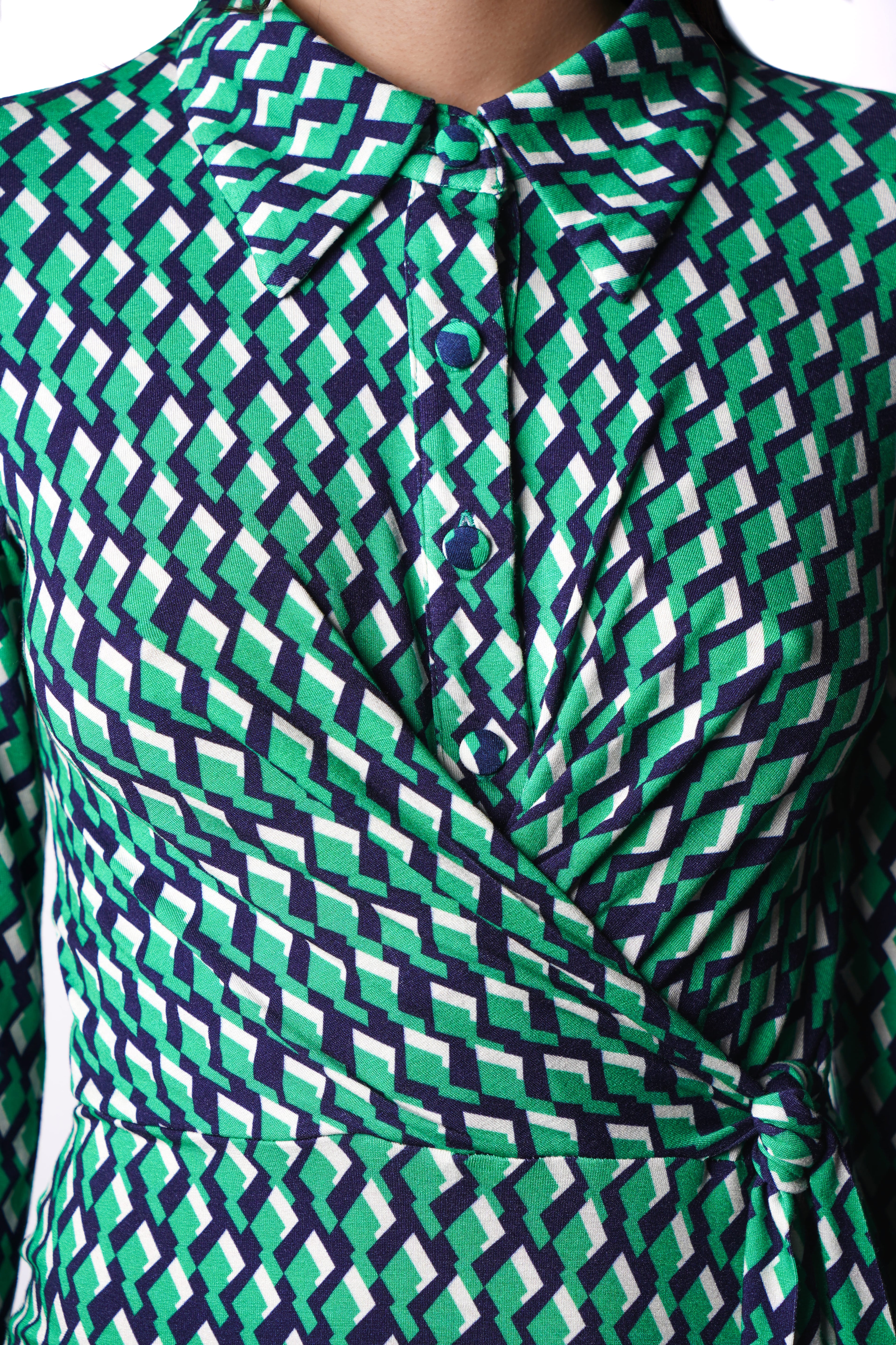 Robe à imprimé vert géométrique mi-longue, coupe fluide et moderne. Col chemisier et boutonnage caché. Drapé croisé sur le côté gauche pour une touche sophistiquée. Bas légèrement évasé. Fabriquée en France.