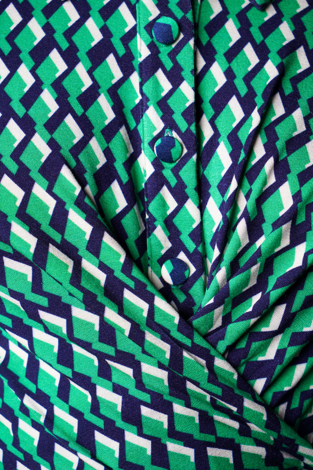 Robe à imprimé vert géométrique mi-longue, coupe fluide et moderne. Col chemisier et boutonnage caché. Drapé croisé sur le côté gauche pour une touche sophistiquée. Bas légèrement évasé. Fabriquée en France.