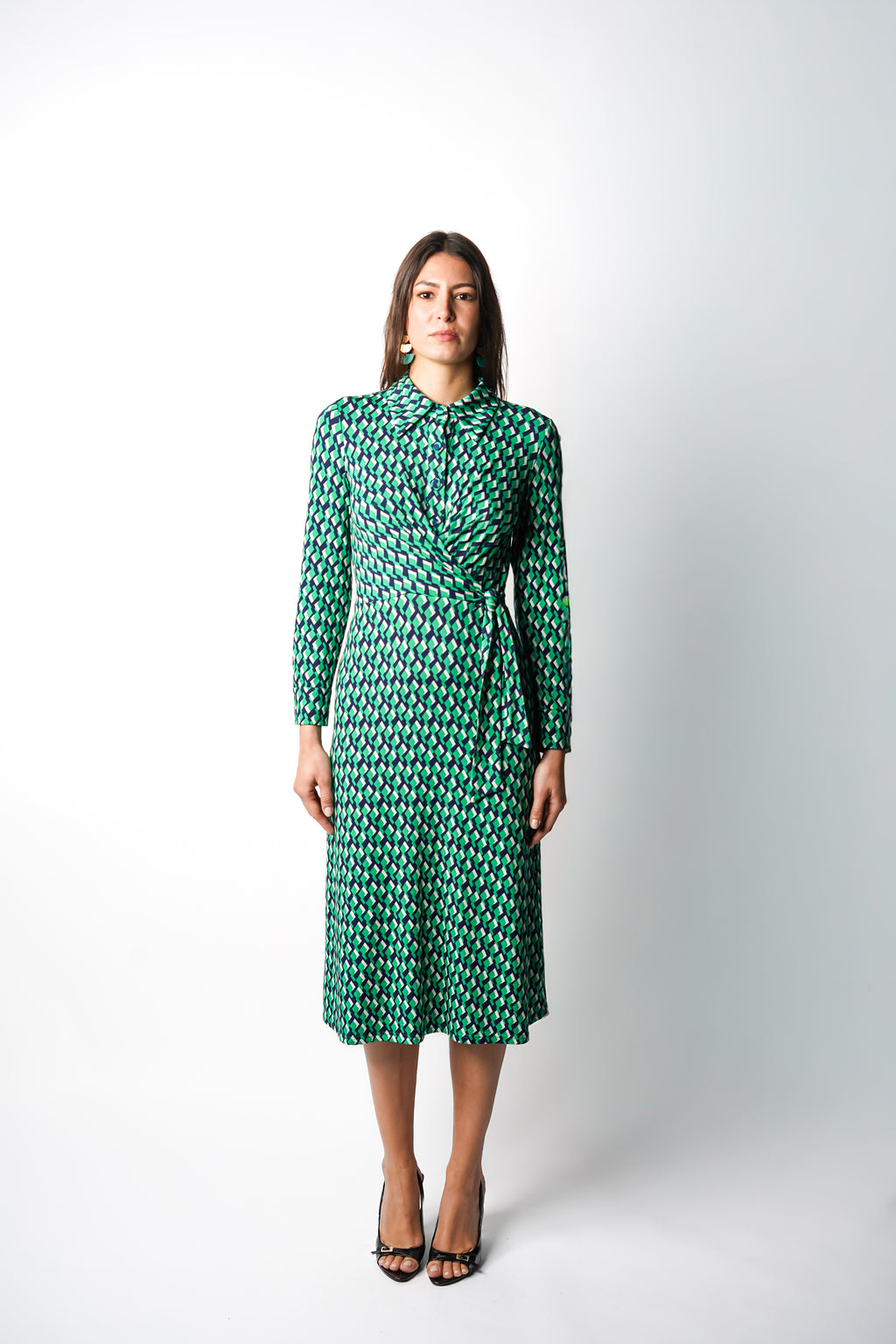 Robe à imprimé vert géométrique mi-longue, coupe fluide et moderne. Col chemisier et boutonnage caché. Drapé croisé sur le côté gauche pour une touche sophistiquée. Bas légèrement évasé. Fabriquée en France.