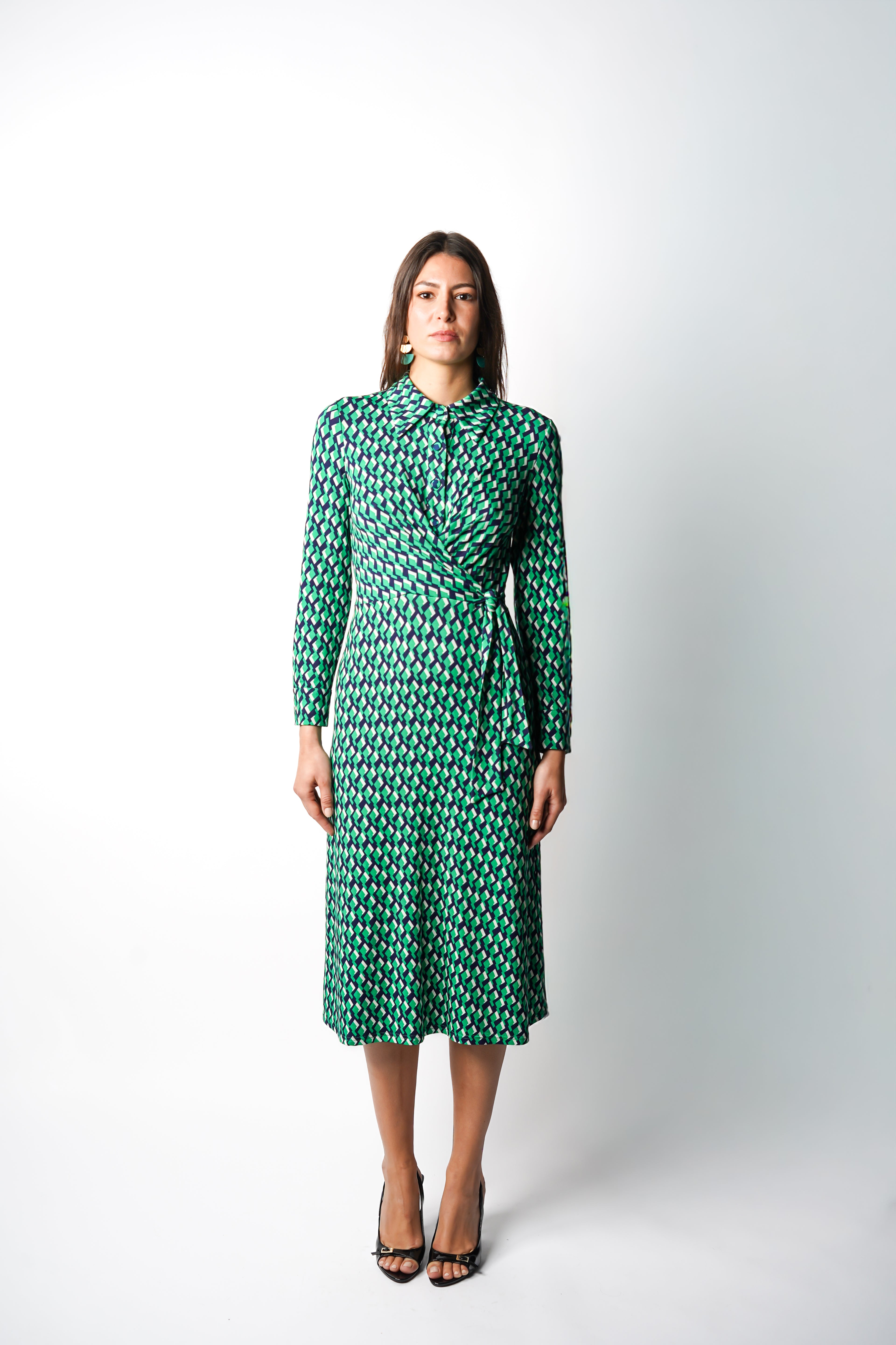 Robe à imprimé vert géométrique mi-longue, coupe fluide et moderne. Col chemisier et boutonnage caché. Drapé croisé sur le côté gauche pour une touche sophistiquée. Bas légèrement évasé. Fabriquée en France.